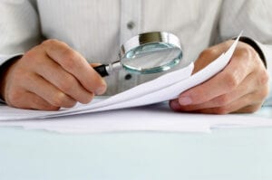 man's hands holding magnifying glass examining documents